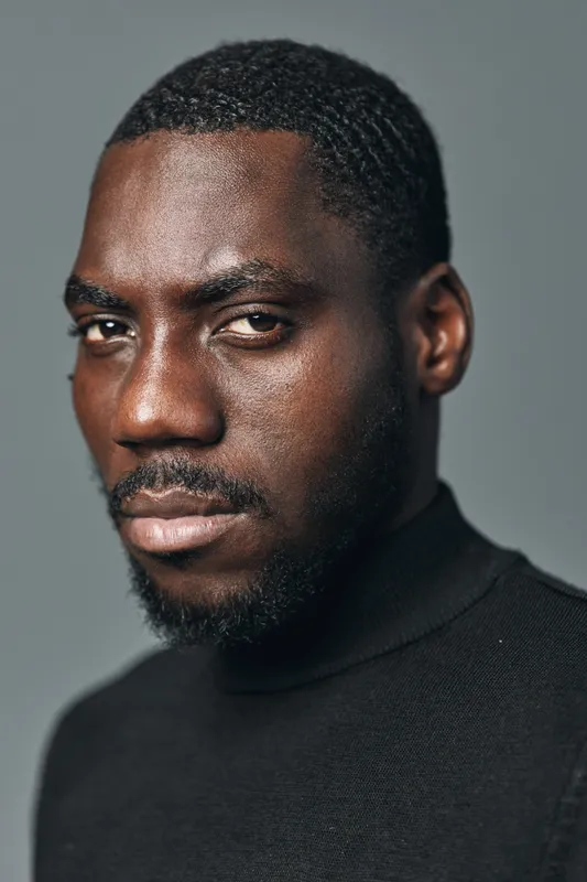 African man portrait with dark skin and short hair wearing black turtleneck sweater in creative conceptual visual style with serious expression on gray background.