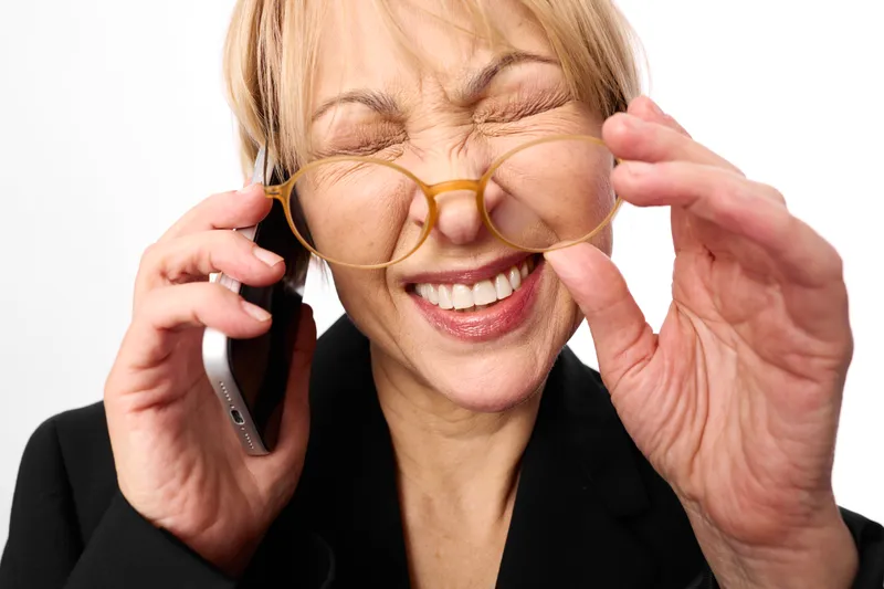 Woman on phone adjusts glasses, stressed anxiety expression, multitasking communication while tired, eyewear business portrait on white background, pressure burnout strain coping