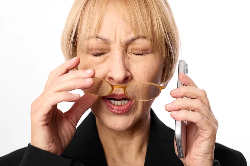 Woman businesswoman phone eating multitasking mobile communication office stress elderly senior blonde suit professional call lunch snack cookie closeup portrait on white background