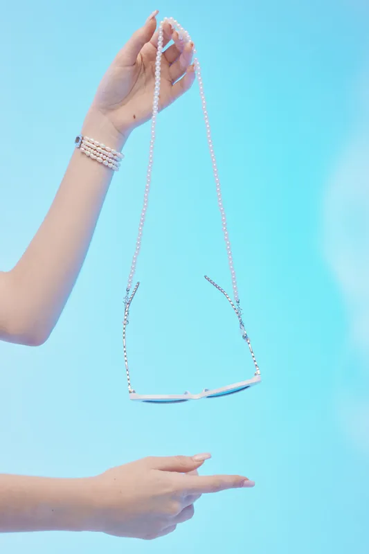 Close-up of a woman holding a stylish sunglasses chain with pearl beads on a blue background. Concept for beauty, fashion, and elegant accessories.