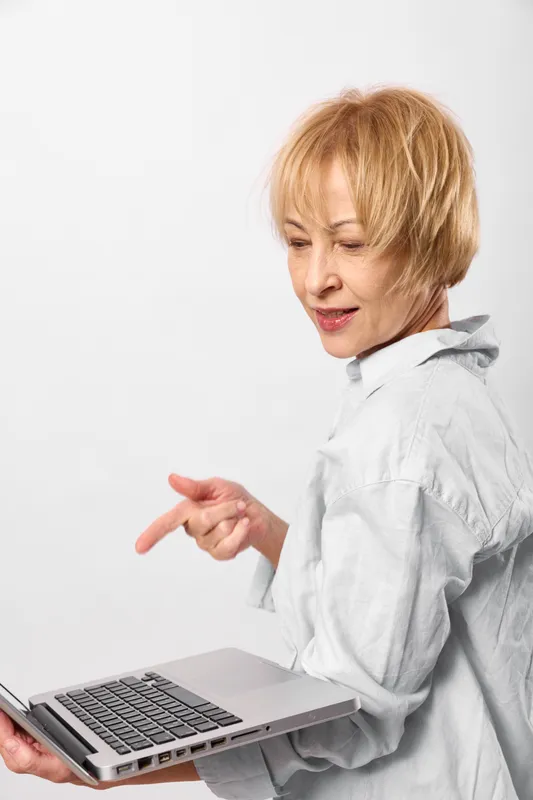 Senior woman with short hair using laptop, typing at desk in studio light, remote work office concept, technology communication online productivity, focus