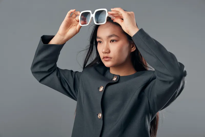 Woman, portrait and fashion with sunglasses on head, wearing dark jacket, studio lighting with gray background for casual style and beauty posing for camera.