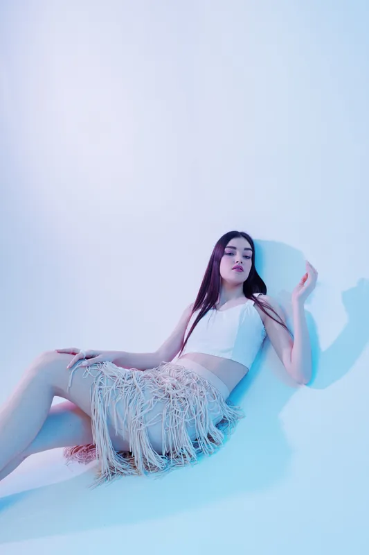 Young woman in stylish fashion outfit poses against a light background. Concept of beauty, fashion, elegance, and modern style for editorial or commercial use.
