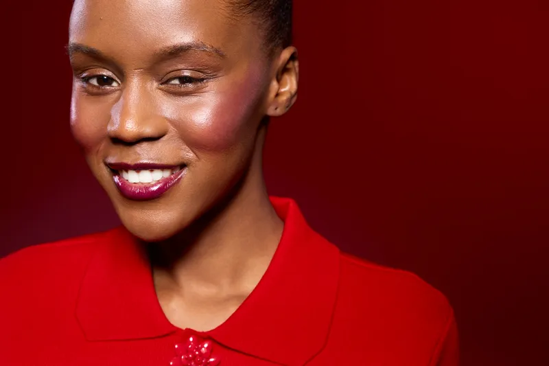 Close-up portrait of a smiling African American woman with dark skin wearing a red outfit. She poses confidently against a red background. Concept of beauty, fashion, and elegance.