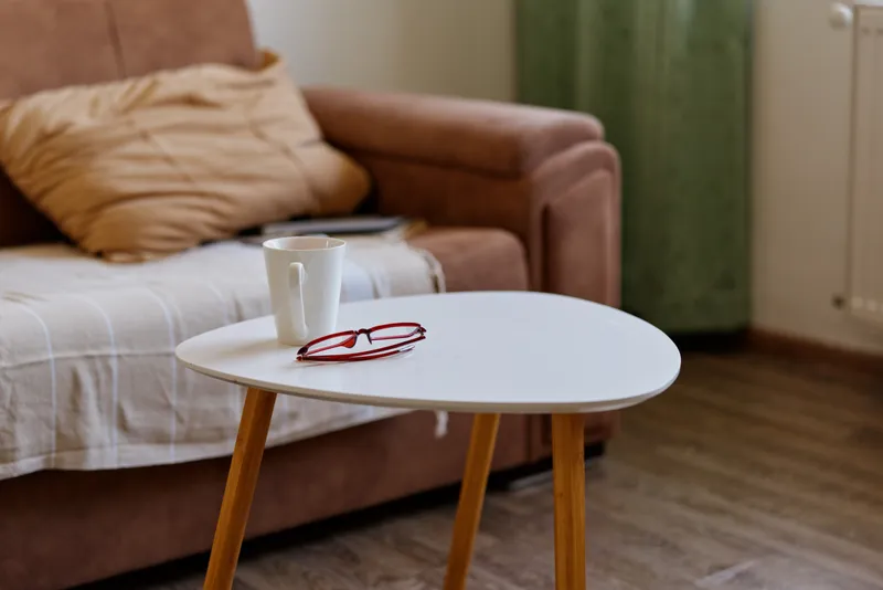A quiet living room scene features a small round table with a mug and red glasses beside a sofa, conveying a calm home lifestyle mood and everyday simplicity.