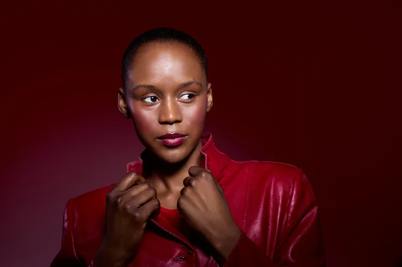 Portrait of a confident dark skinned African woman wearing a red leather jacket against a red background. Concept of fashion, beauty, empowerment, and modern style.