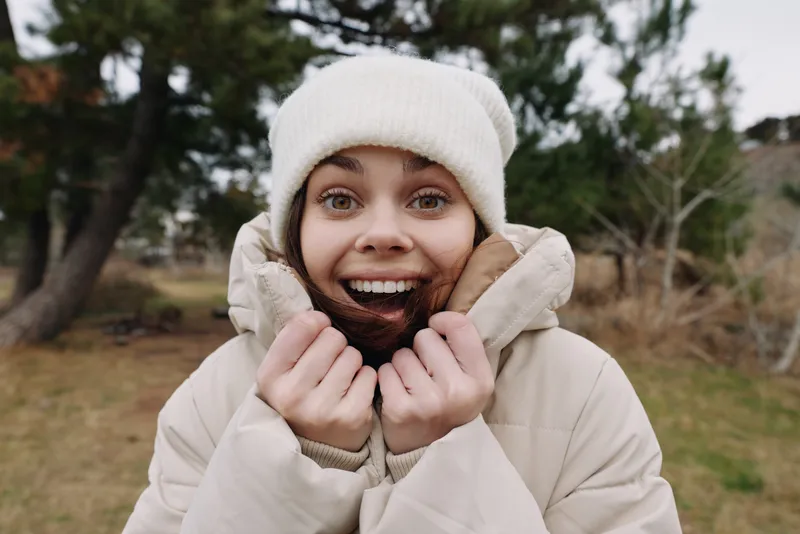 Woman in winter outerwear outdoors, smiling warmly, wearing a cozy beanie and jacket, enjoying cold weather and fresh air in a natural outdoor setting suitable for stock