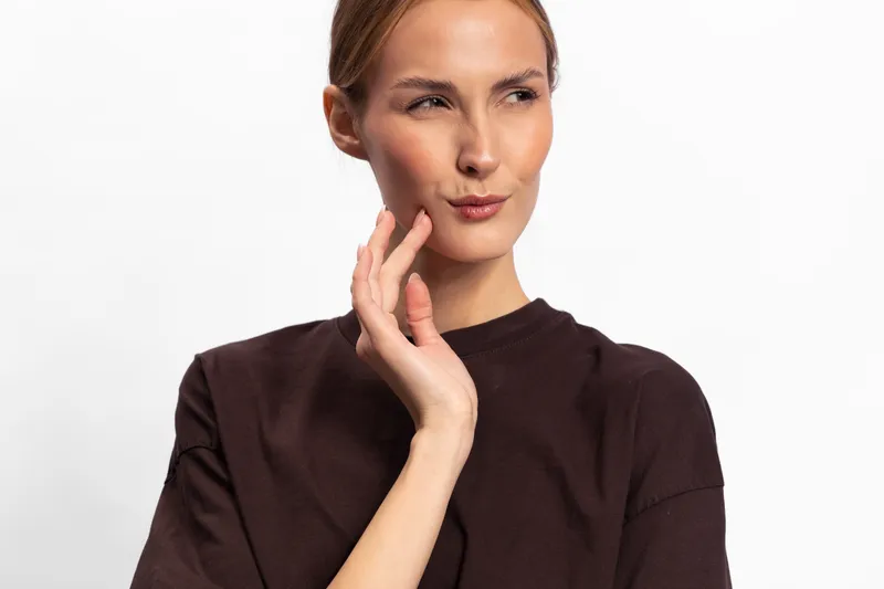 Thoughtful woman with fair skin and light hair wearing a dark brown sweater looks aside with a pensive expression on white background. Concept for contemplation and decision making.