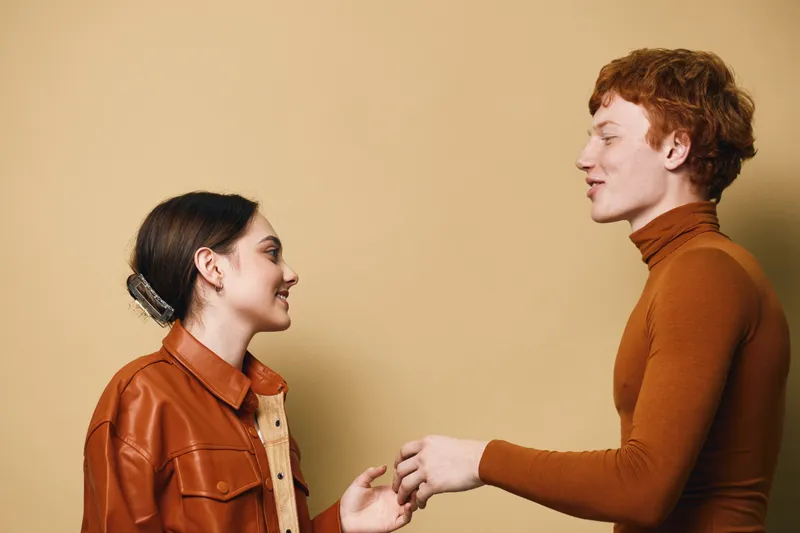 Young man and woman smiling and shaking hands in casual clothes with neutral background for friendship, communication and connection in studio portrait.
