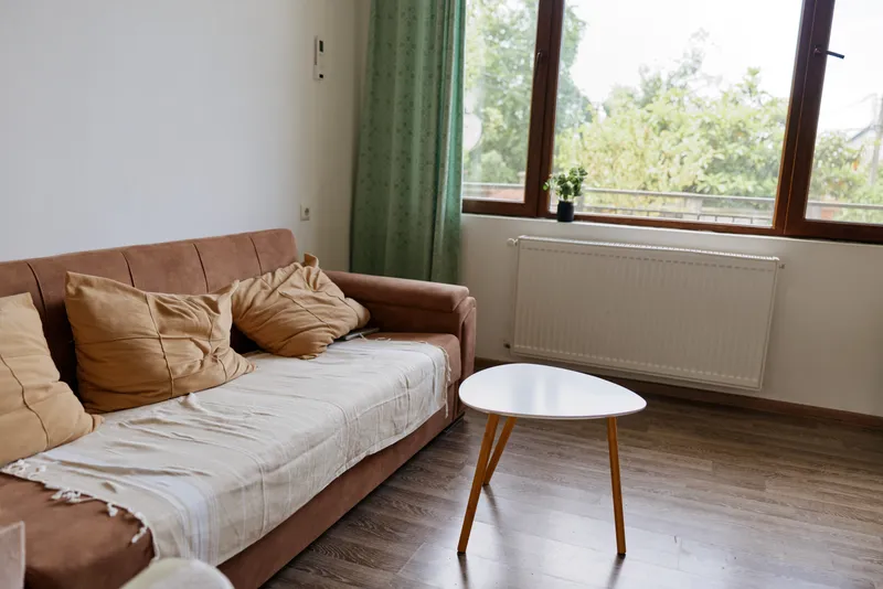 Cozy living room scene with a light brown sofa and a small round table by a bright window, conveying calm, homely comfort and a simple relaxed mood.