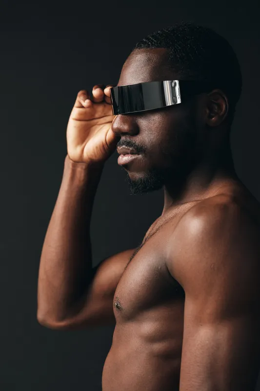 Creative conceptual portrait of African man with dark skin wearing futuristic visor glasses in visual style on black background. Artistic, modern and innovative male model.