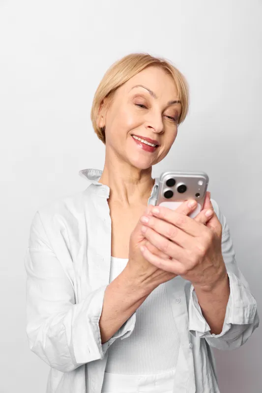 Woman smiling senior holding smartphone, close portrait on white background, casual home style, communication and social media, soft studio light