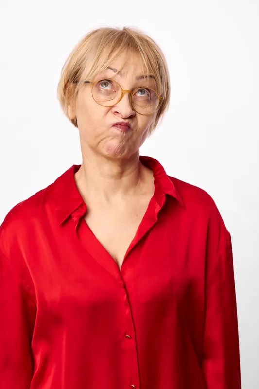 Senior woman with glasses in red shirt, studio portrait on white background, serious thoughtful expression, looking to side, plain lighting, copyspace