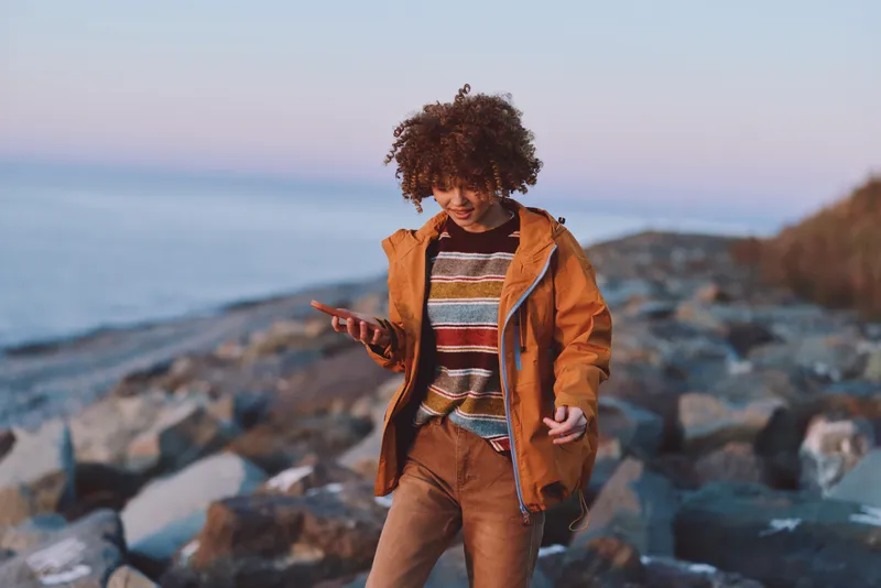 Woman lifestyle, seaside rocks at sunset, casual jacket and sweater, woman walking outdoors, warm evening light, travel mood, looking at camera