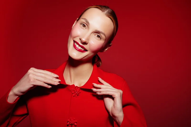 Smiling woman in red sweater poses against red background, showing joyful expression and confident mood. Concept of fashion, beauty, happiness, and vibrant style in studio lighting.
