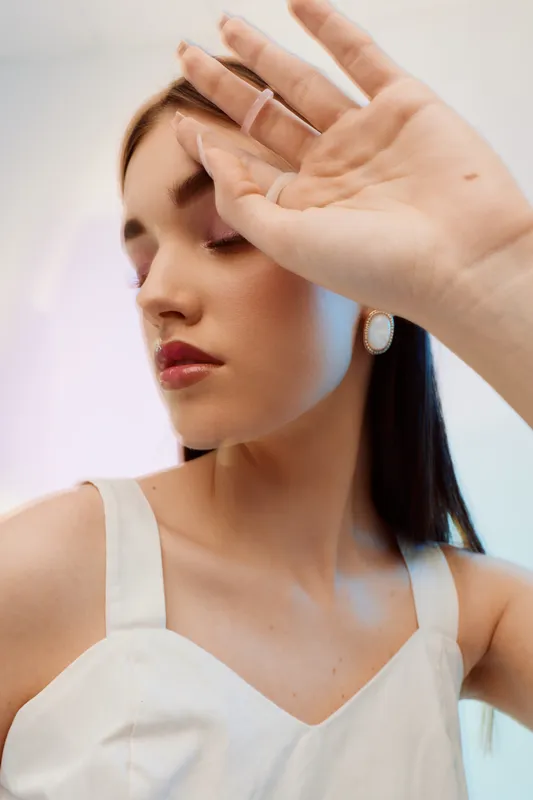 Young woman with closed eyes and natural makeup poses with hand raised near face. Soft lighting highlights her beauty and fashion style. Concept for elegance and skincare.