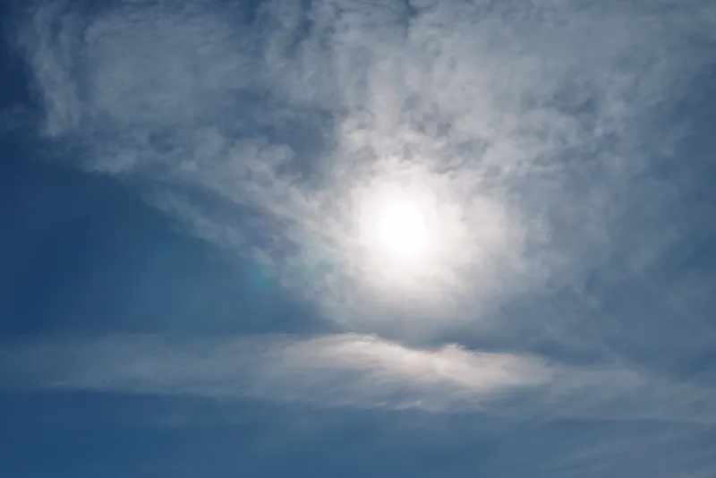 Bright sun high in a clear blue sky with wispy clouds, casting warm light across the atmosphere and creating a serene daytime scene suitable for nature, weather or outdoor mood shots.