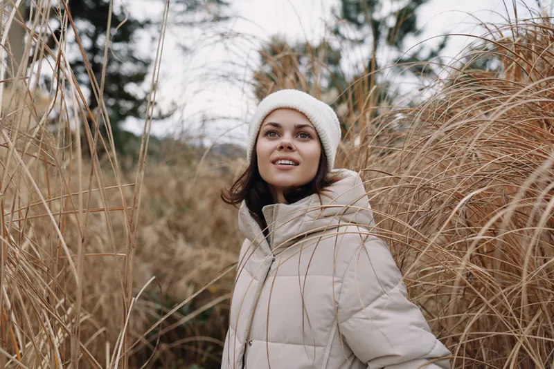 Winter woman outdoors portrait in a padded coat beside tall dried grass, a calm scene with soft light and serene natural texture and mood.