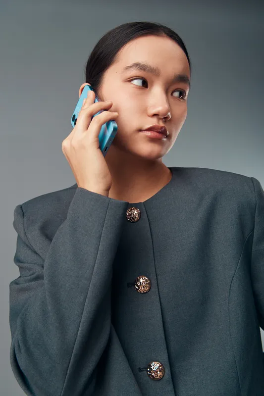 Young woman in gray jacket talking on smartphone looking sideways with serious expression isolated on gray background. Communication, technology and connection concept with person.