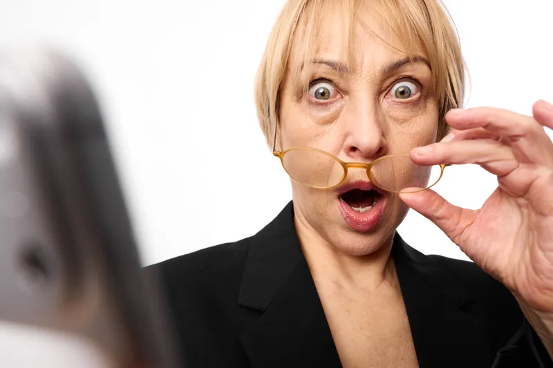 Surprised woman shocked expression in office, blonde hair, open mouth and finger gesture near lips, watching computer screen, concept of news surprise, communication anxiety