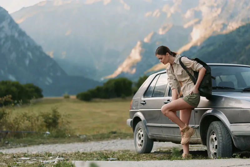 woman lifestyle outdoors, stepping from car in sunlit field, mountains in background, backpack ready, candid moment, relaxed posture, fresh breeze, natural colors, joyful mood