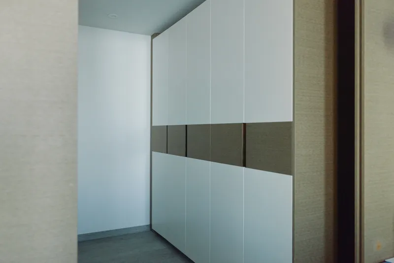Wardrobe and closet system along a minimal hallway with clean lines, white doors and subtle shadows creating organized storage.