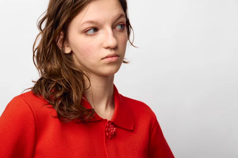 Young woman in red sweater looks away with a serious expression on white background. Concept of contemplation, emotion, and casual fashion portrait with natural light.