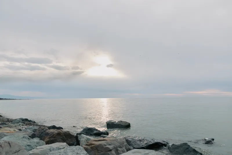 Calm sea landscape with rocky shore under cloudy sky. Soft light reflects on water surface creating peaceful atmosphere. Concept of nature, serenity, and coastal environment.