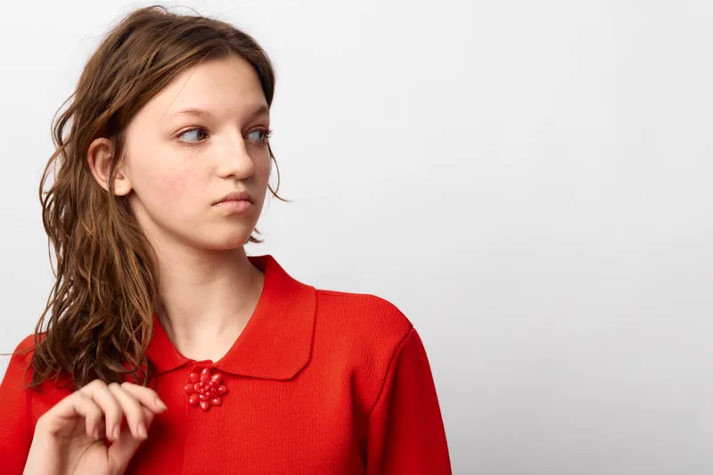 Young woman in red sweater looks to the side with thoughtful expression. Studio portrait on white background. Concept of contemplation, fashion, and casual style.