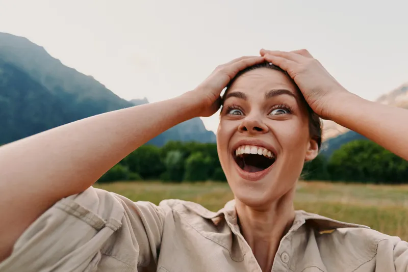 Vibrant woman outdoors, smiling with joy, lifestyle oriented scene amid nature, happiness and carefree energy in a sunlit field with distant mountains
