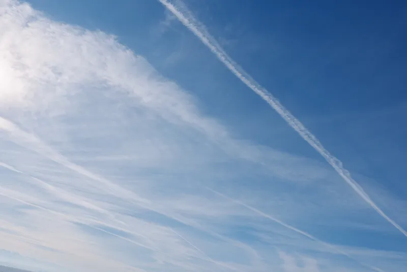 Blue sky with wispy clouds and white contrails crossing the horizon, capturing open space and aviation mood for landscape and travel themed photography