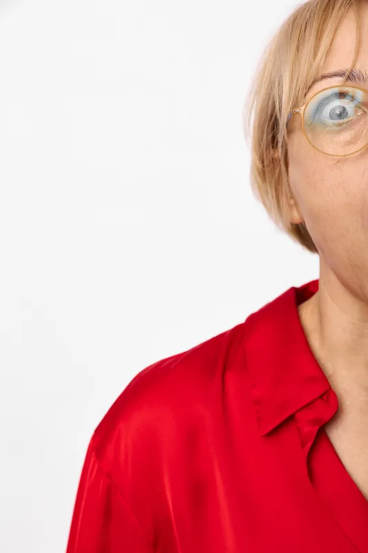 Woman with glasses, closeup portrait, blonde hair, red shirt, cropped face, bright studio light, white background, calm smile, minimal style, soft focus clarity