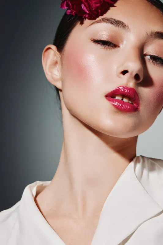Close-up of young woman with pink lips and subtle glowing skin, wearing white outfit, artistic fashion makeup styling under soft shadows, beauty portrait concept.
