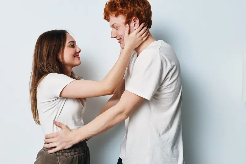 Young couple, woman and man in casual clothes embracing, smiling and looking at each other on white background for love and relationship concept.