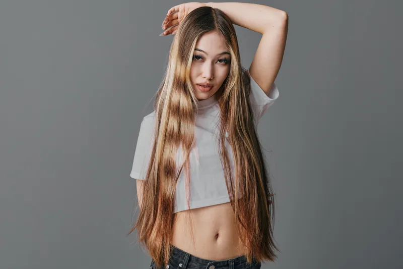 Young woman with long straight hair posing in casual crop top and jeans against gray background. Beauty, fashion and style concept with confident expression and relaxed pose.