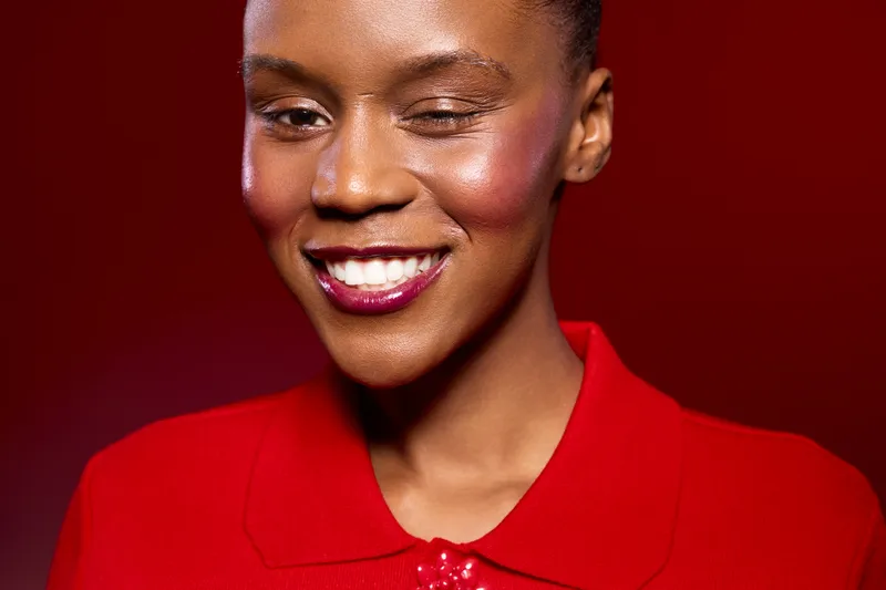 Smiling African American woman with dark skin winks and wears bright red clothing against a red background. Concept of happiness, confidence, beauty, and fashion portrait.