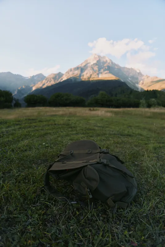 Backpack resting on a grassy meadow with distant mountains under a clear blue sky. Outdoor adventure mood, exploring nature, and quiet travel vibes.