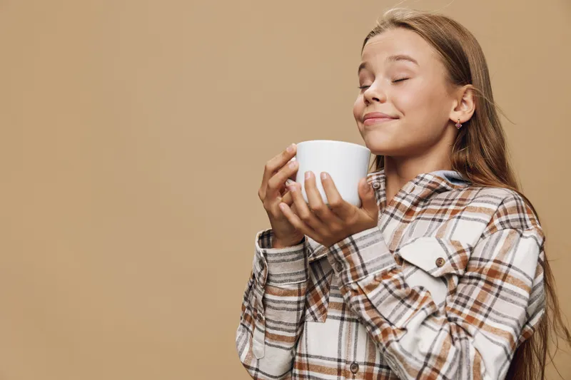 Young woman enjoying a hot beverage with eyes closed in cozy plaid shirt against beige background for relaxation and calm moment at home.