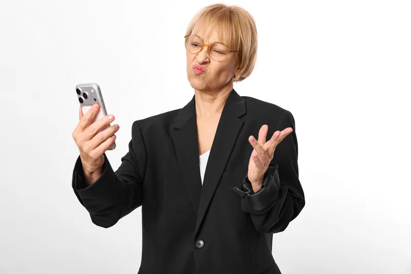 Businesswoman with smartphone showing surprise and upset reaction, woman in blazer, business communication gesture toward technology, isolated on white background