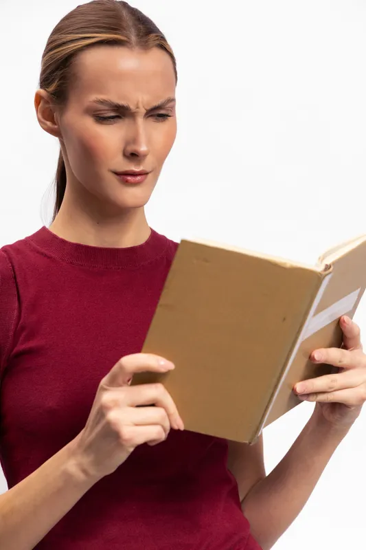 Confused woman in red sweater reading book with furrowed brows and focused expression. Isolated on white background. Concept for concentration, confusion, knowledge, and study.