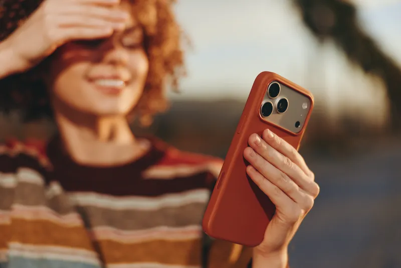 woman lifestyle outdoors smartphone selfie smiling portrait summer technology communication, curly haired woman holding mobile camera, sunshine, relaxed smile, blurred city background