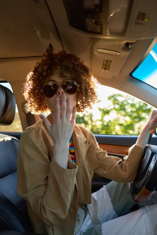 Curly haired woman wearing sunglasses in a car, candid lifestyle moment with retro film color tones and warm, vibrant lighting inside the cabin.
