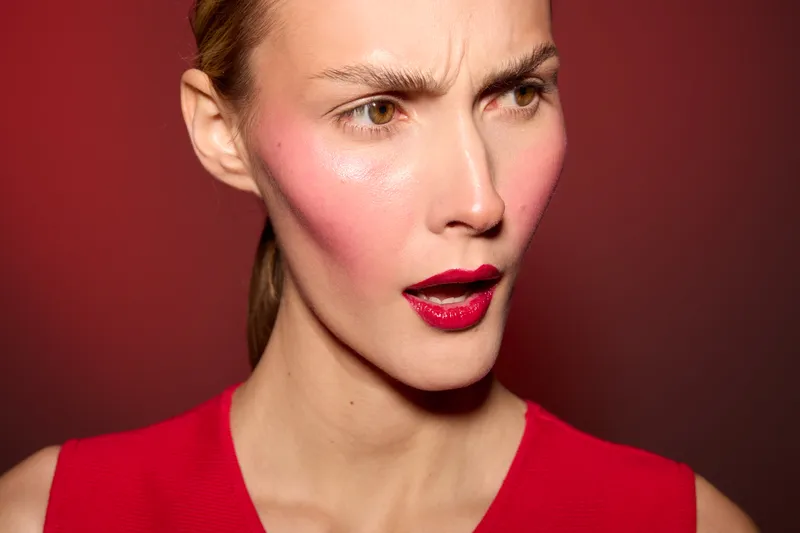 Close-up of a confused woman with red lipstick and flushed cheeks wearing a red top against a red background. Concept for emotion, surprise, and beauty portrait.