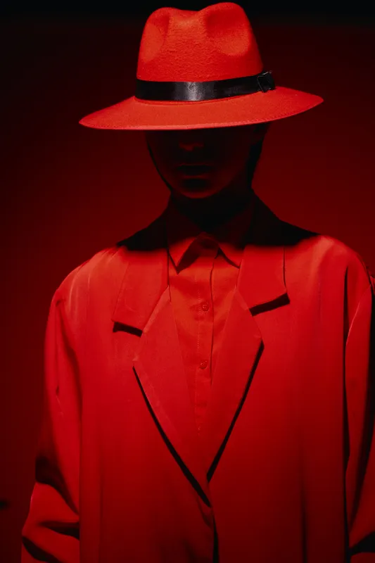 Silhouette of a fashionable person wearing a red hat and matching oversized coat in dramatic lighting. Creative concept for fashion, beauty, and bold style visuals.