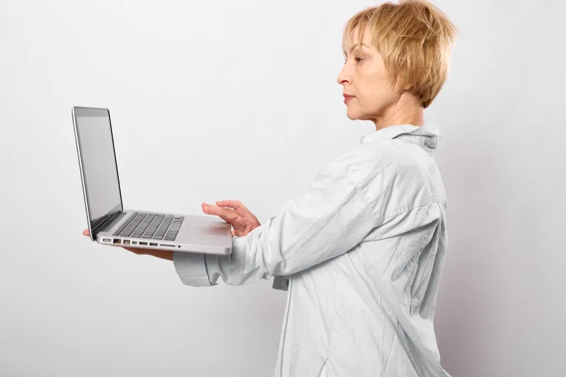 Senior woman with short hair works on laptop, typing in profile, remote at home on a bright white background, technology for learning and digital communication