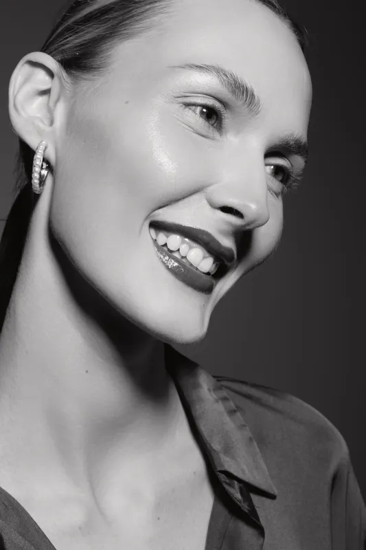 Smiling Caucasian woman with light skin wearing a shirt and hoop earrings looks sideways in black and white studio portrait. Concept of happiness and beauty.