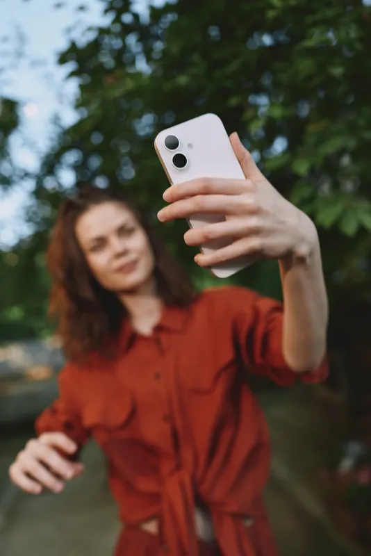 Smiling woman in a red dress taking a selfie outdoors with a smartphone. daylight, green trees in the background, lifestyle and fashion vibe, casual and upbeat mood