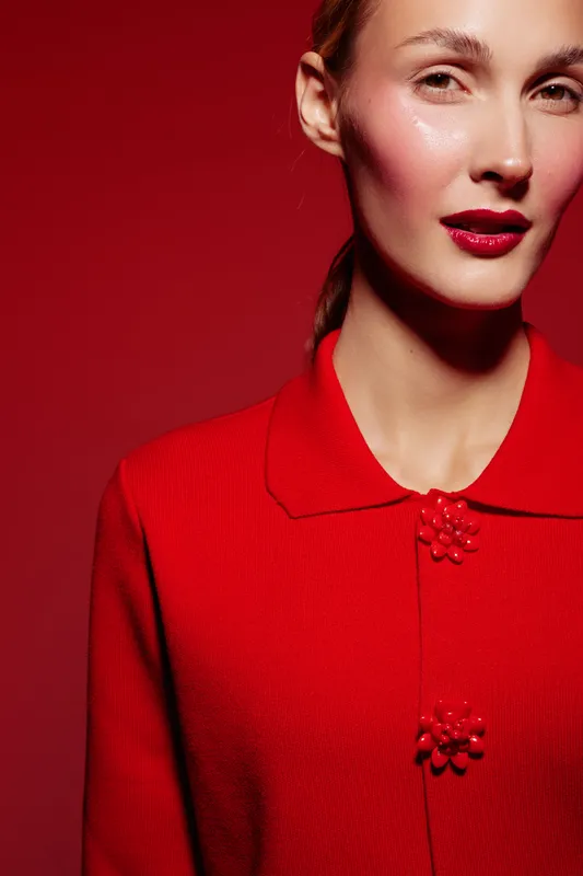 Close-up portrait of a woman wearing a red textured jacket with decorative buttons against a red background. Concept of fashion, elegance, and monochrome style.