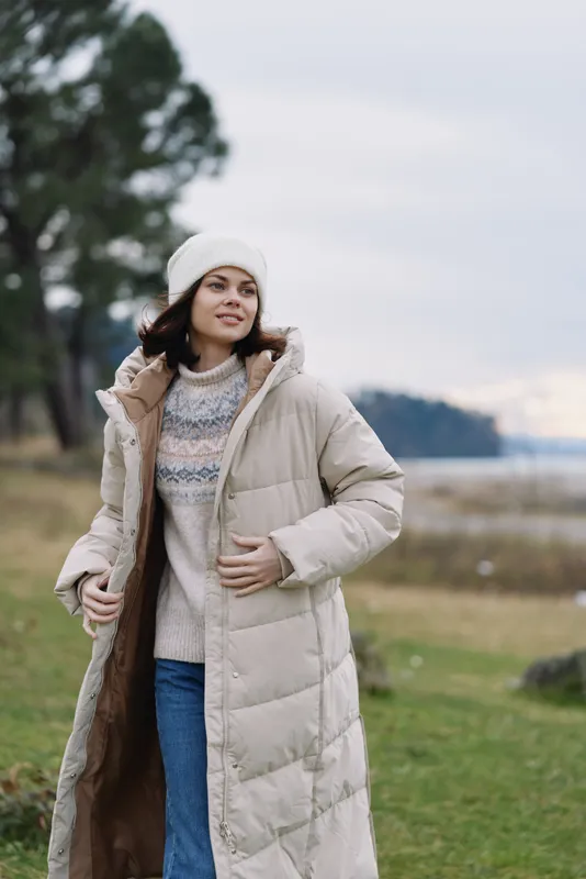 Winter woman wearing a long beige coat in a park, cozy knit sweater and beanie, calm pose with soft natural light, showcasing outdoor fashion and lifestyle in chilly weather