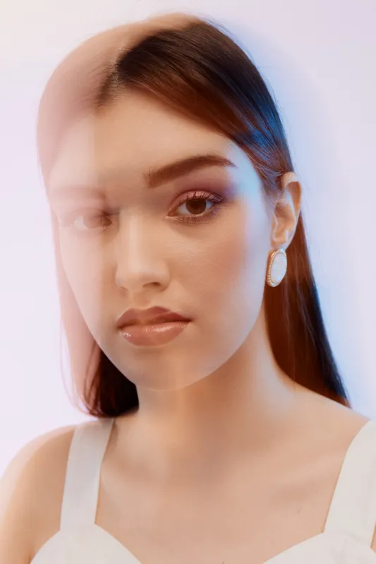 Young woman beauty fashion portrait with glossy lips and earrings looking at camera. Soft lighting and blurred double exposure effect on neutral background. Concept for style.